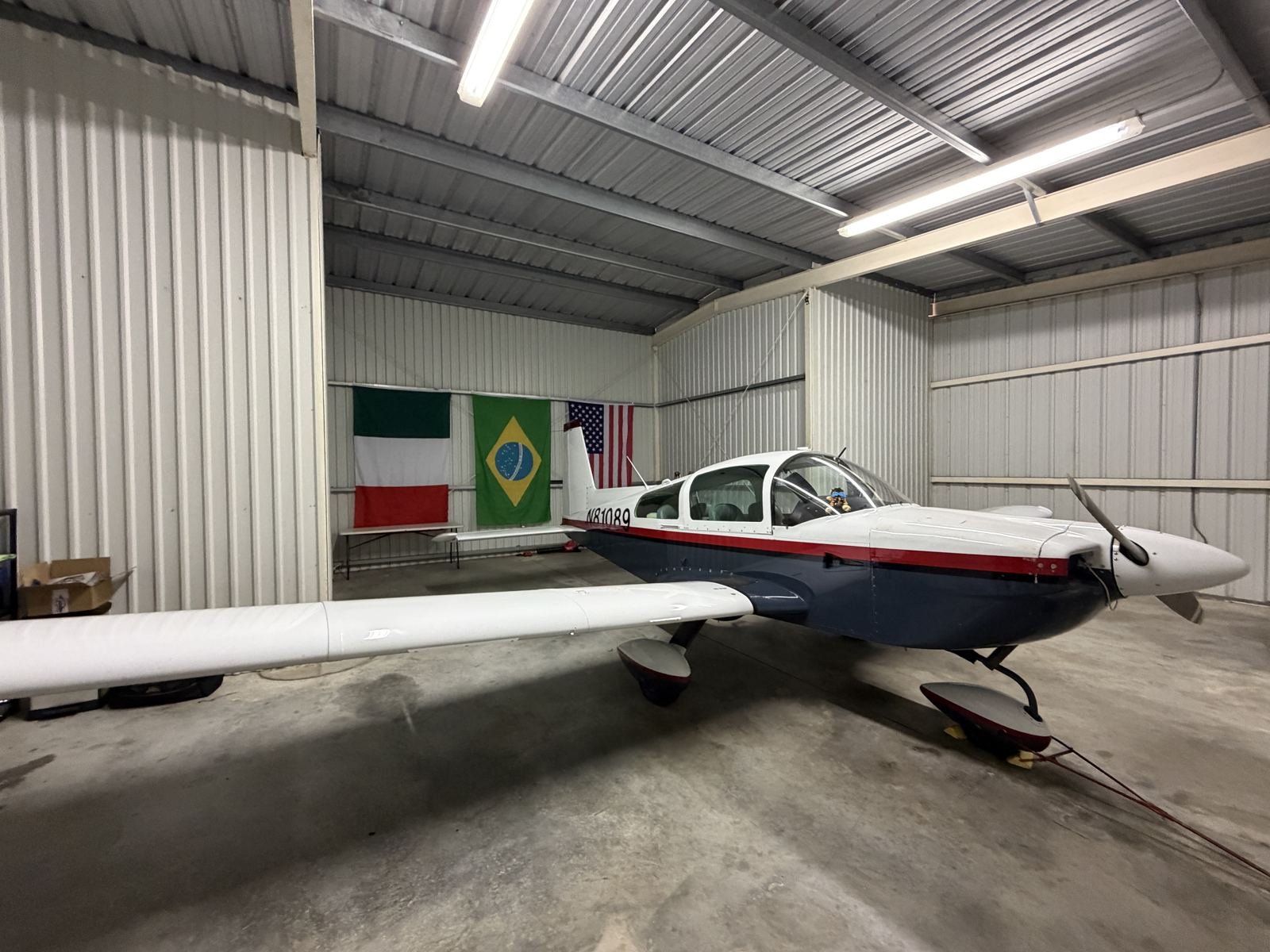 N81089, FFS Air's Grumman Tiger, in its hangar in front of Italian, Brazilian and American flags